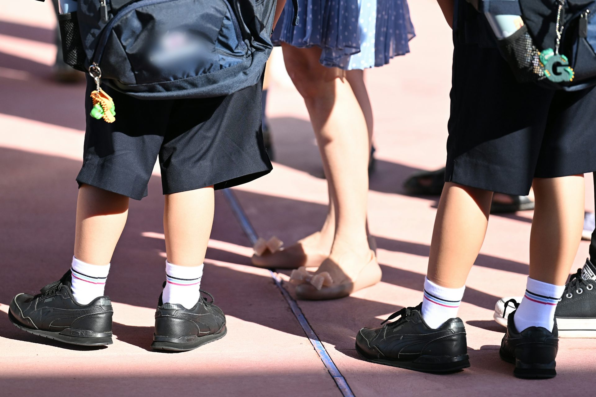 Two children in uniform stand outside with an adult.