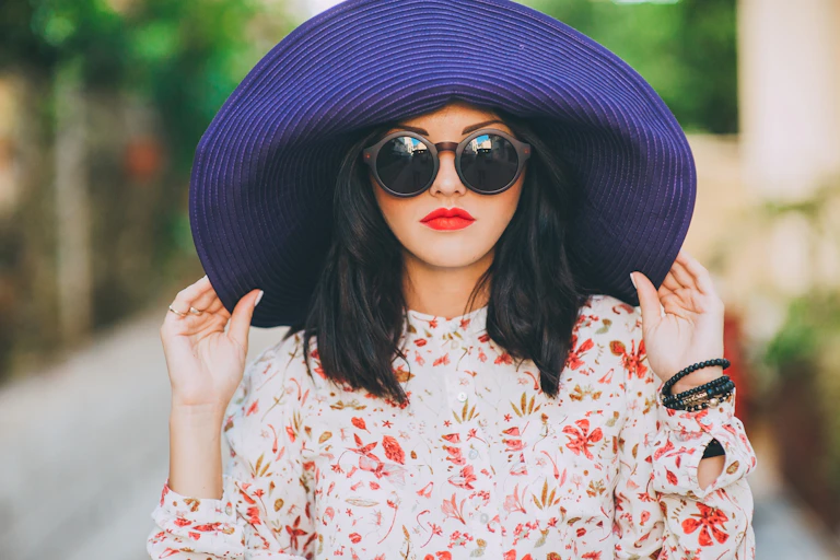 A fashionable woman wears sunglasses and a big hat.