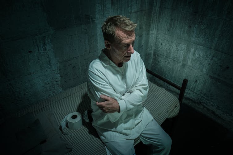 Film still: a man sits alone in a cell.