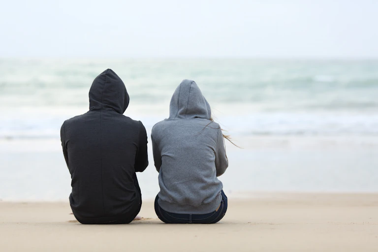 Teens in hoodies sat facing the sea