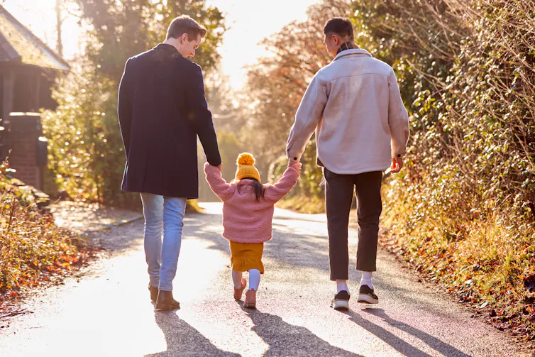 Dads seen walking a toddler by the hands.