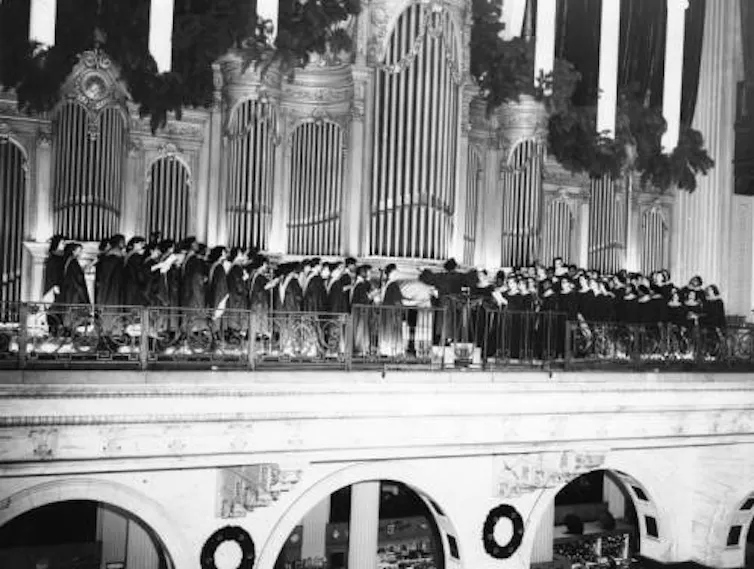 Black and white photo of choir permforming in front of massive organ