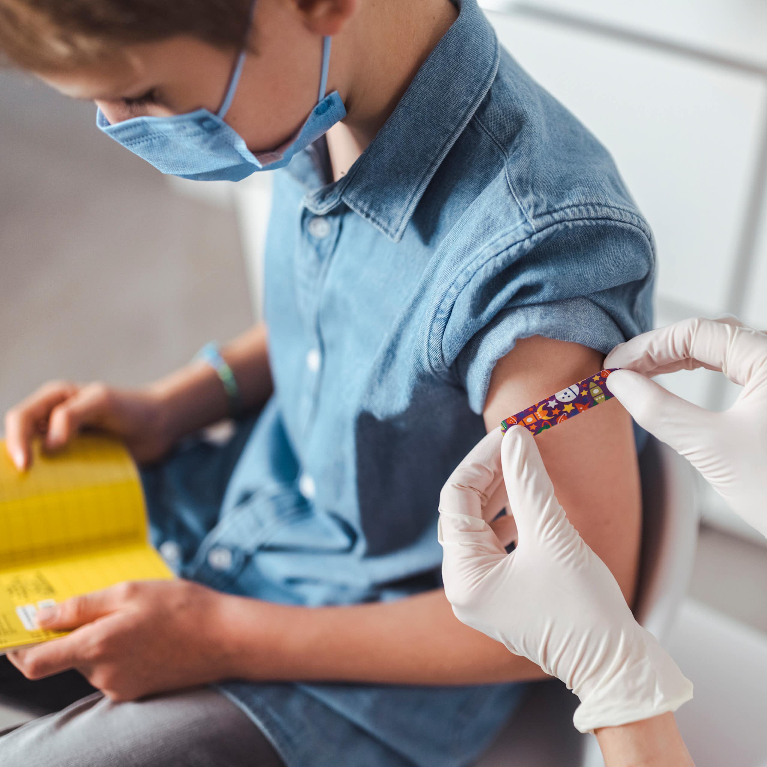 Child looking down at vaccine record while clinician puts bandaid on their arm