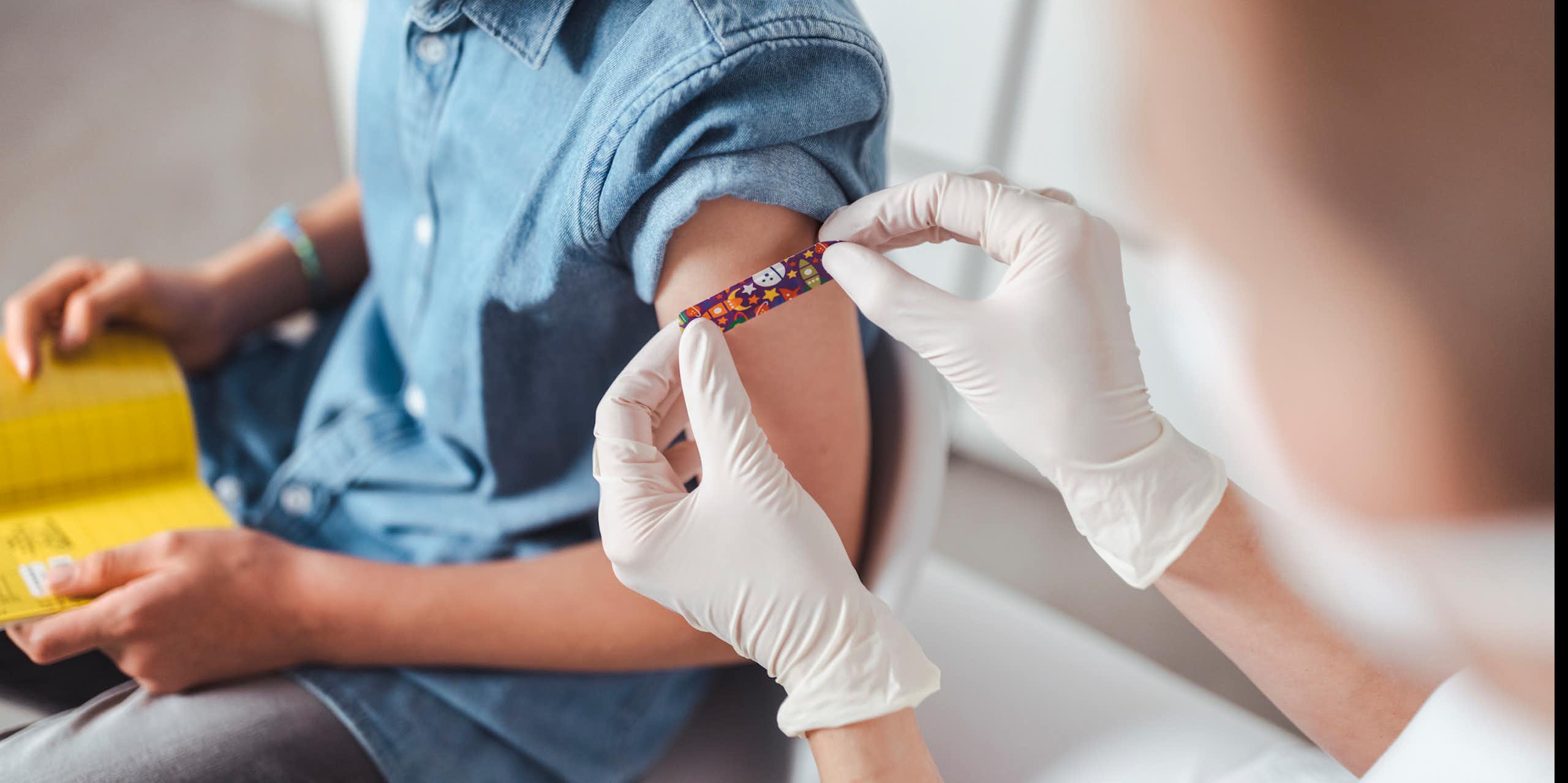 Child looking down at vaccine record while clinician puts bandaid on their arm