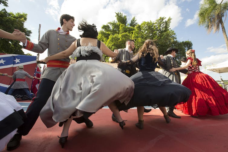 Dancers in antebellum southern cosutmes on a stage emblazoned with Confederate flag