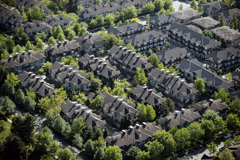 Aerial view of rows of identical townhouses with grey roofs with rows of deciduous trees separating them