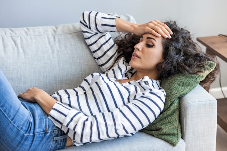 Une femme allongée sur un sofa met sa main sur le front.