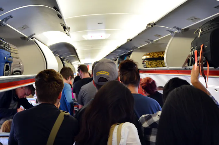 People in the aisle of a plane opening the overhead lockers