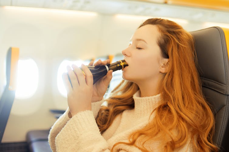 A woman on a plan drinks wine straight from a small bottle