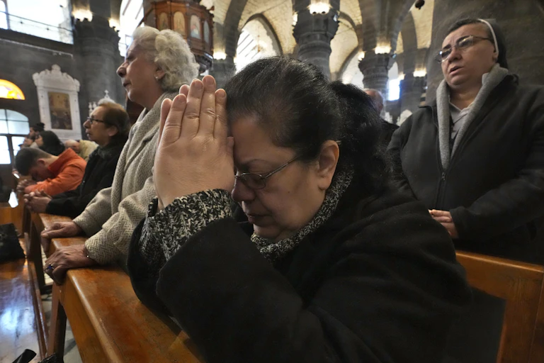 Several people standing in pews, with some joining their hands in prayer and bowing their heads in devotion.