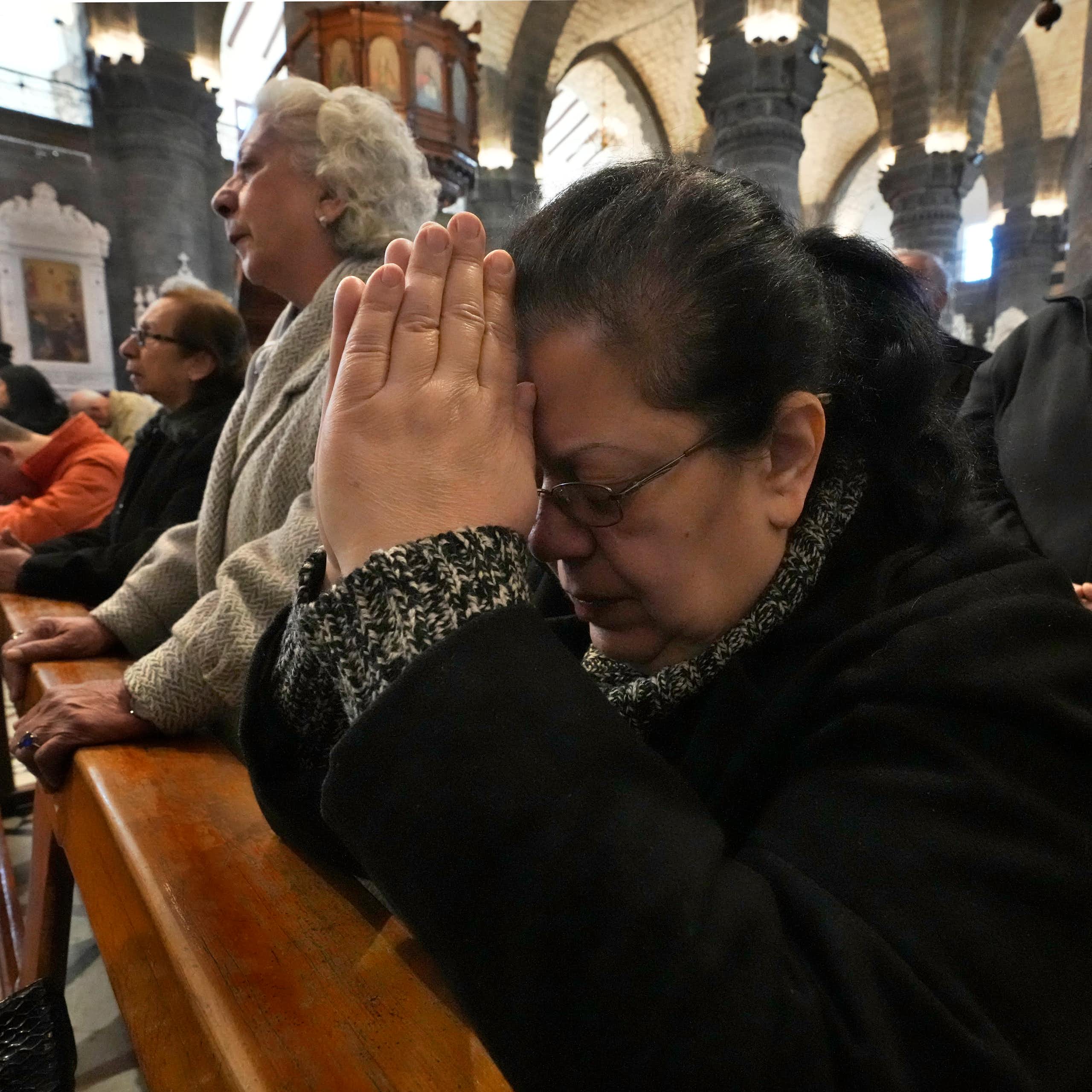 Several people standing in pews, with some joining their hands in prayer and bowing their heads in devotion.