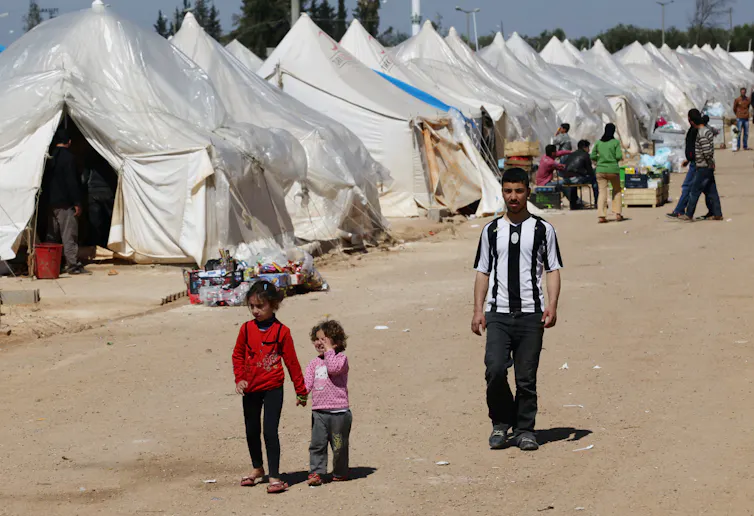 A man and two children walk next to a row of tent encampments.