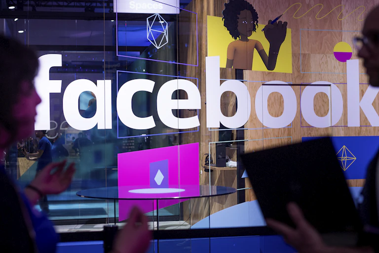 People holding computers and mobile phones walk in front of a Facebook-branded booth.
