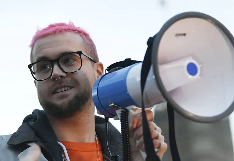 Man with pink hair speaking into a megaphone.