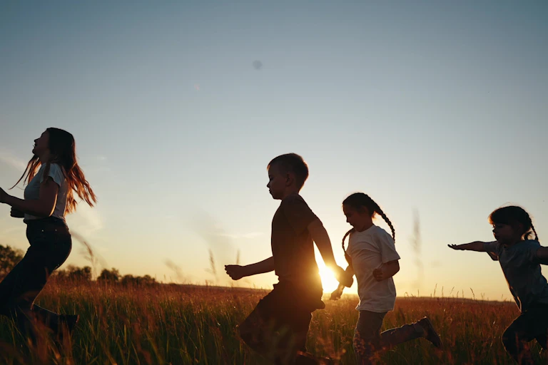 Children running through a field at sunset