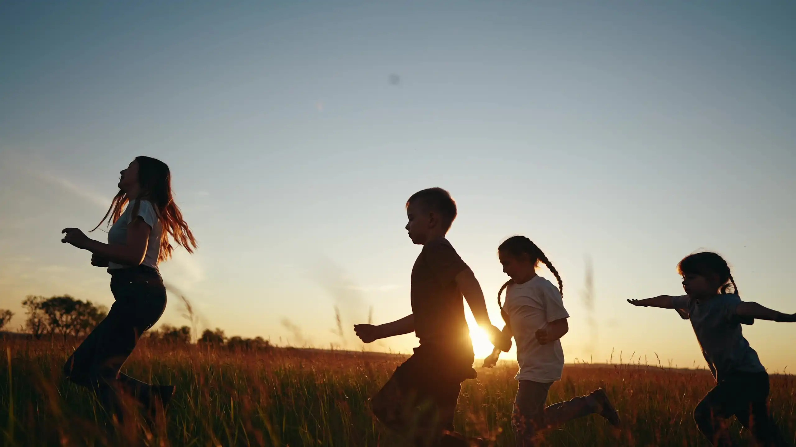 Children running through a field at sunset