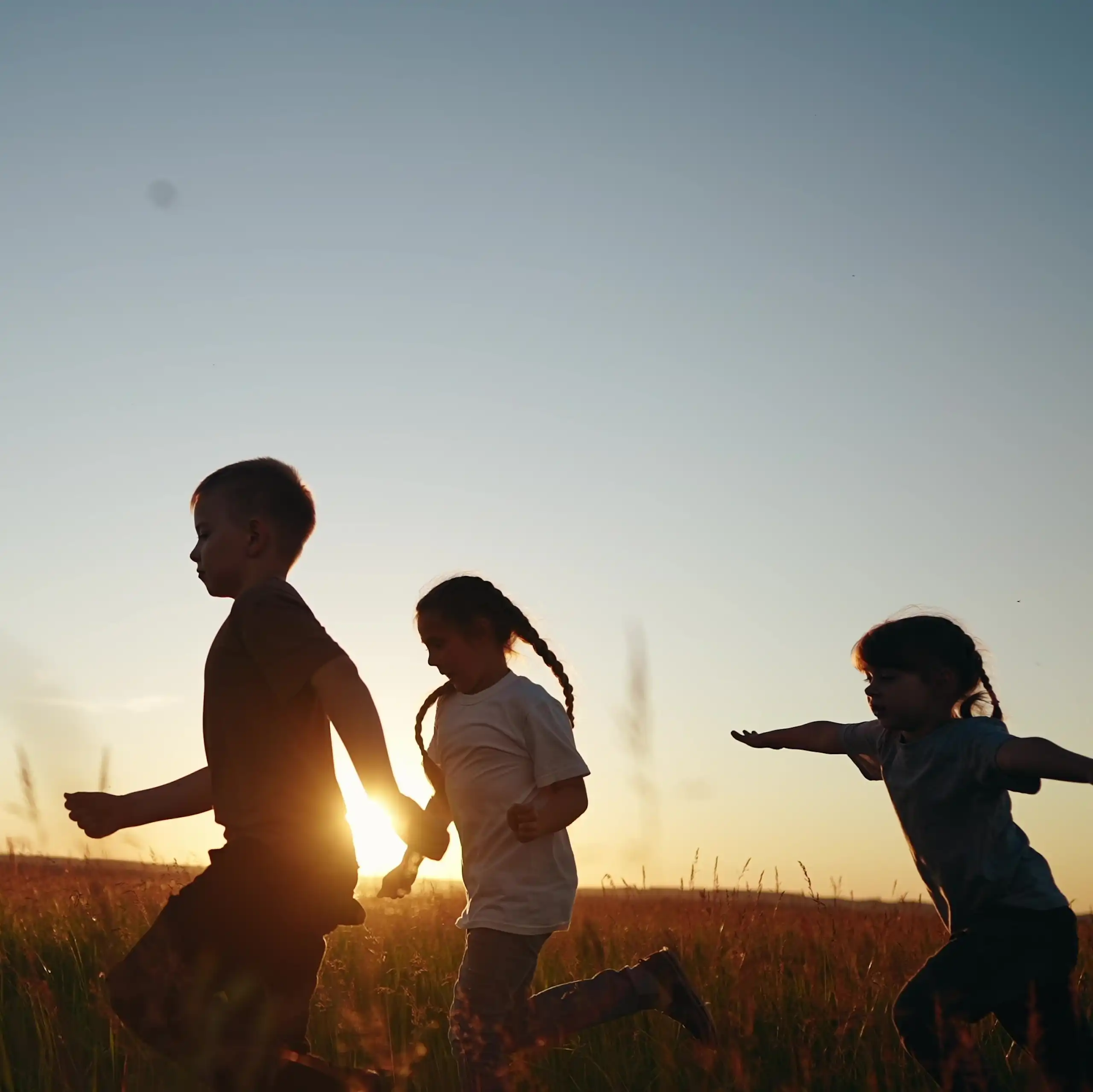 Children running through a field at sunset