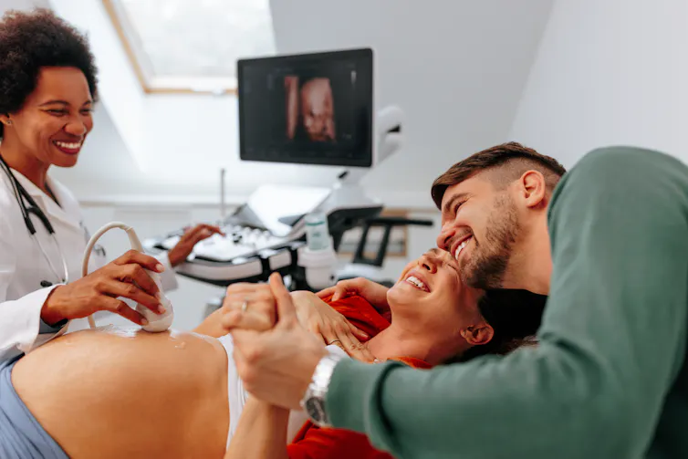 A happy pregnant woman is at the doctors office having an ultrasound scan checkup done with her husband.