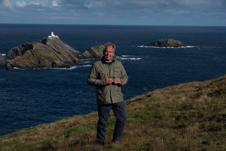 Pen Hadow standing with binoculars at rugged coastal cliff