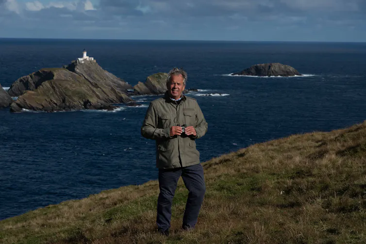 Pen Hadow standing with binoculars at rugged coastal cliff