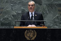 A white man with thinning grey hair stands behind a United Nations lectern.