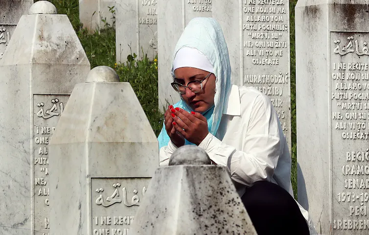 A woman in Bosnian dress holds her hands to her face, surrounded by gravestones.