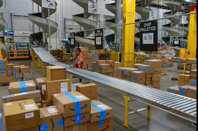 A worker stands by a roller belt in a large warehouse.