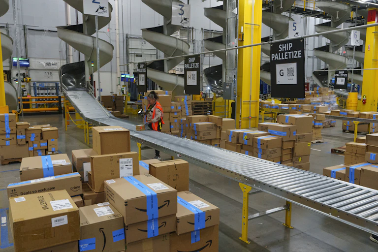 A worker stands by a roller belt in a large warehouse.