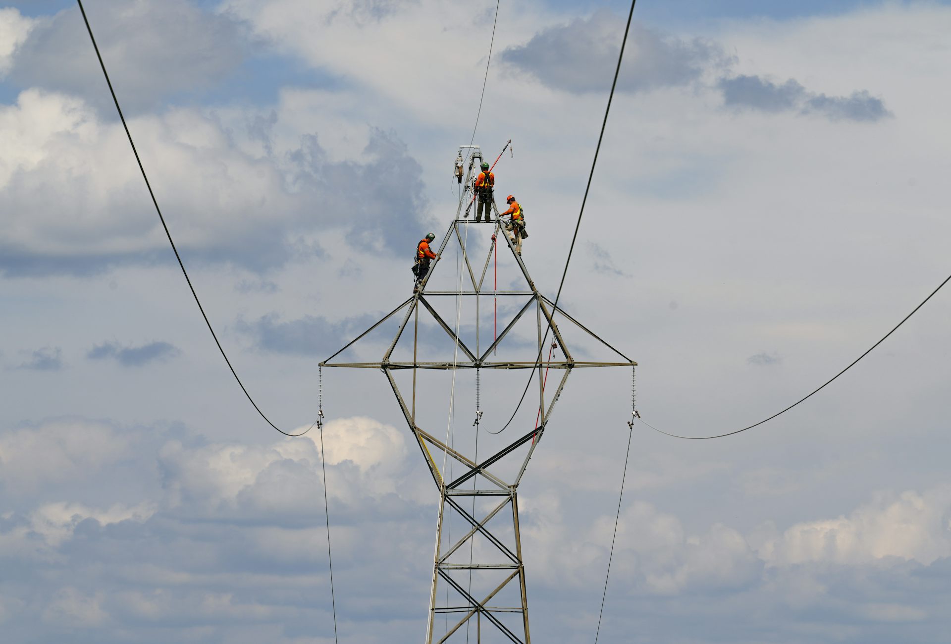 Three Hydro workers on a high power line against a partly cloud sky.
