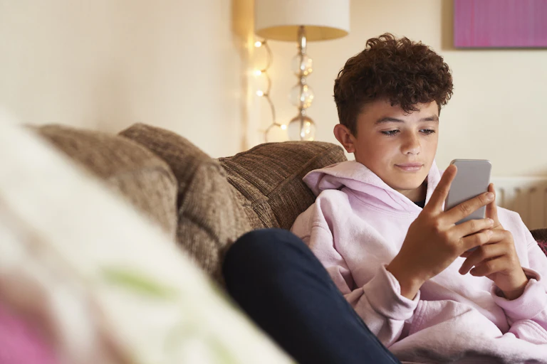 A teenage boy, sitting on a sofa, looks at his phone.