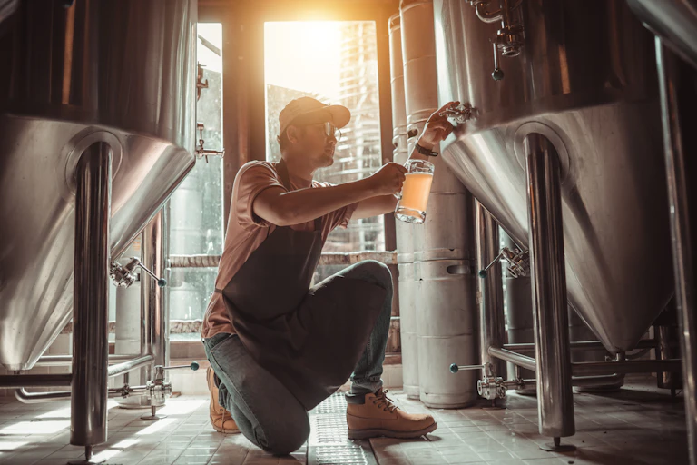 Man on bended knee pours beer from a brewing tank into a beer mug