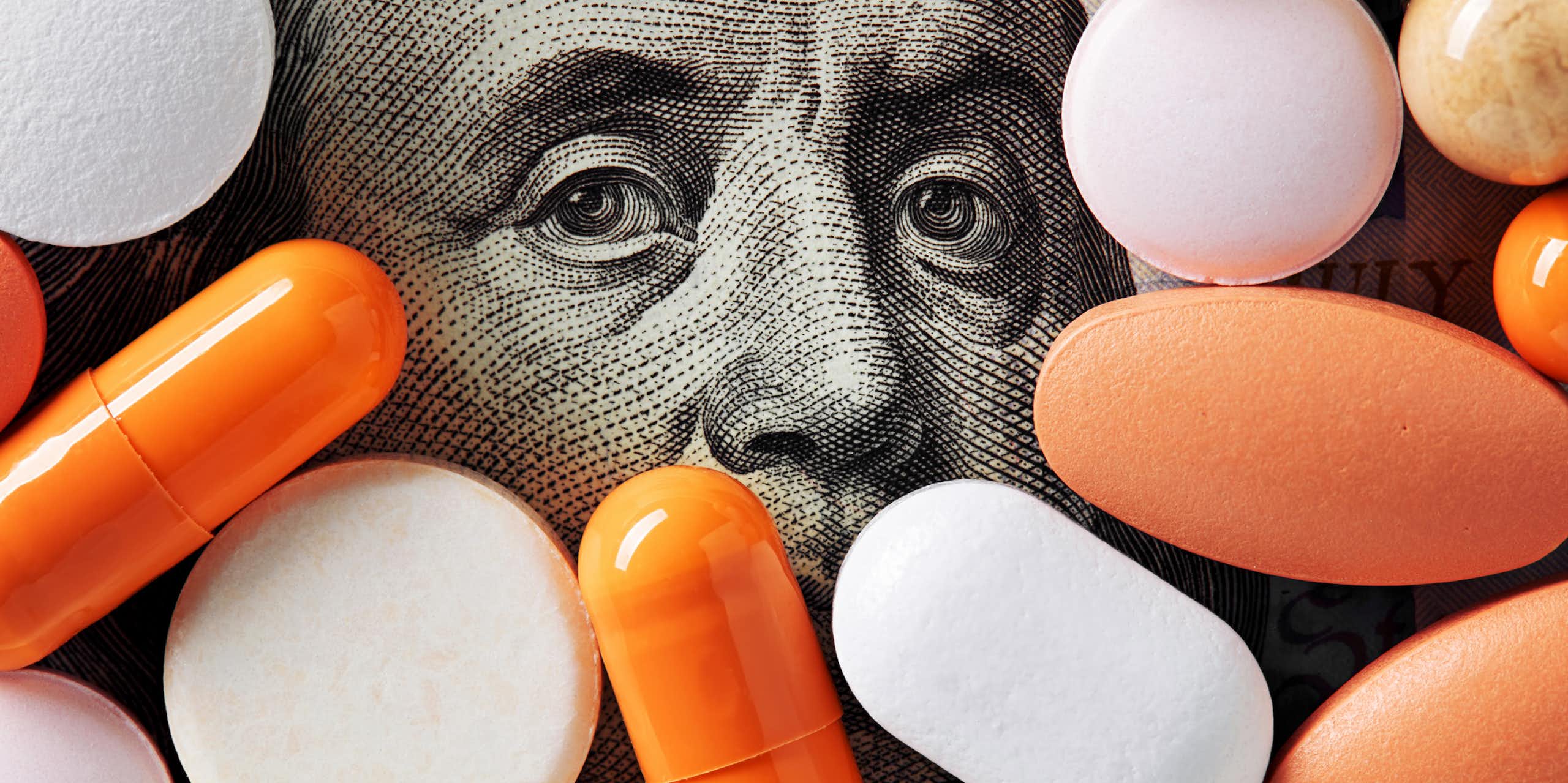 Assortment of pills covering all but the top half of Benjamin Franklin's face on 100 dollar bill