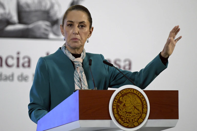 A woman in a neck scarf and green blazer speaks at a lectern.