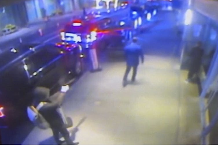 An image from a security video shows a man in a hoodie aiming a gun at another man's back.