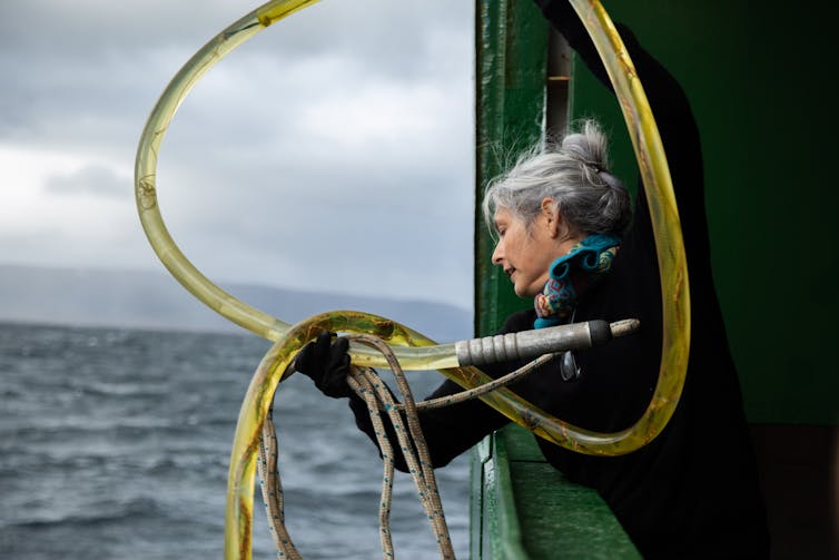 woman with yellow piping - deploying marine survey equipment from side of boat into sea