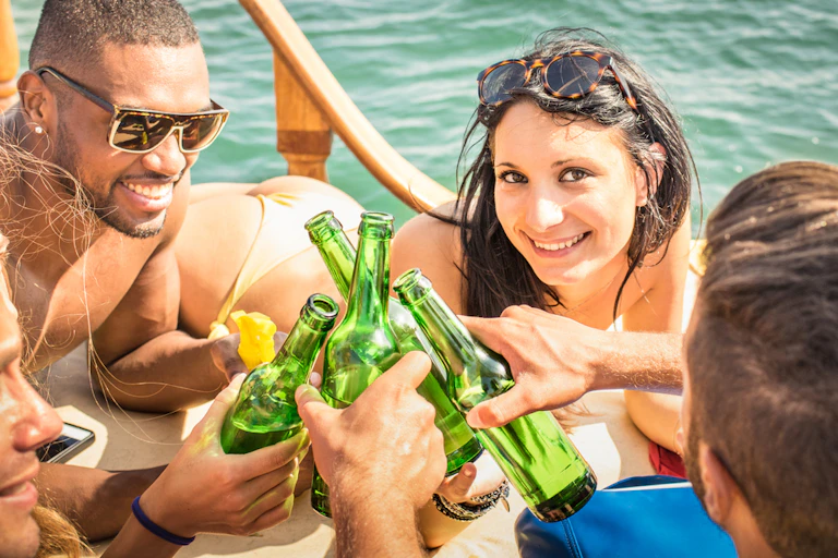 Young adult men and women clinking beer bottles on board boat, woman smiling at camera