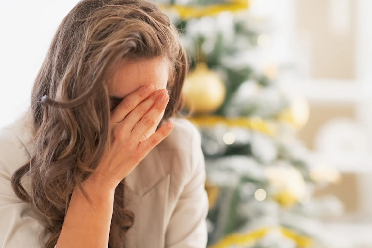 A woman holding her head in her hands in front of a Christmas tree