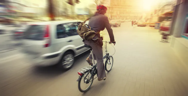 A car passes a cyclist quickly on the road.