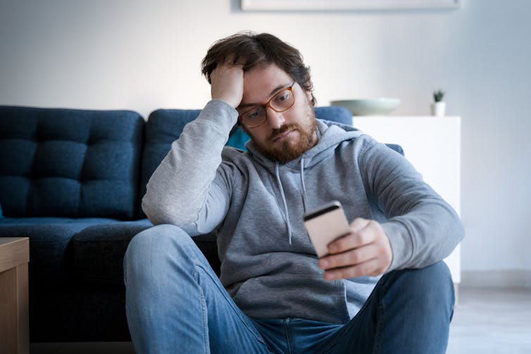 A man looking very upset with his head in his hand, looking at a smartphone