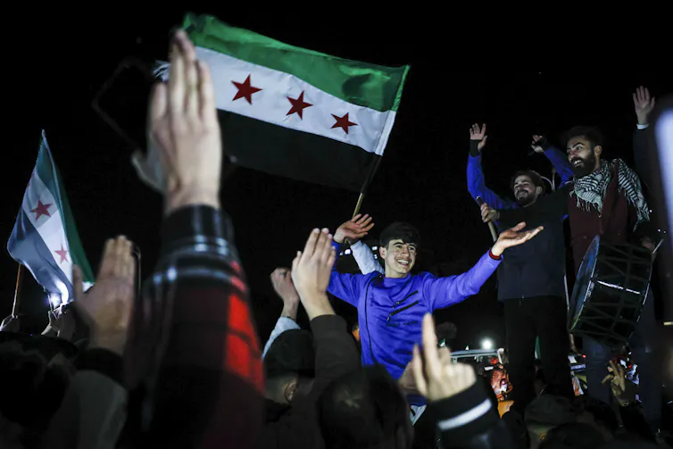 A crowd of Syrians celebrate holding Syrian opposition flags.