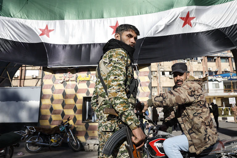 Fighters on patrol in front of a Syrian opposition flag.