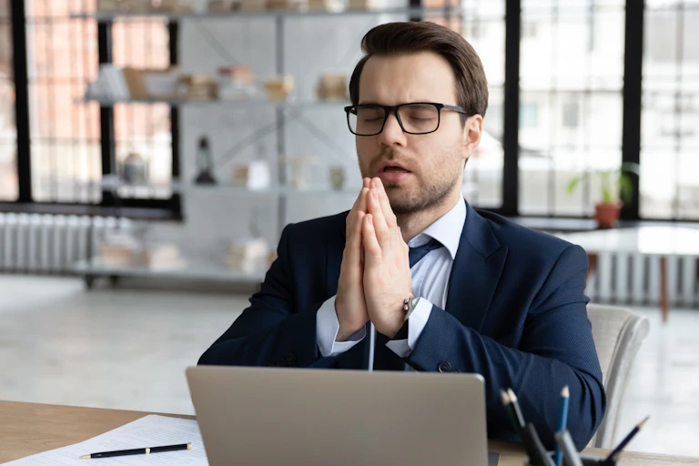 un homme au travail, avec les yeux fermés et les mains jointes dans un environnement de bureaux