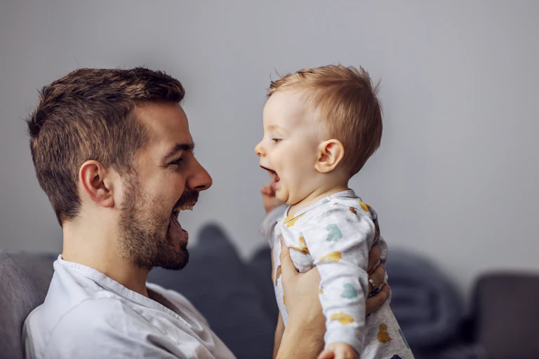 A man holding up a baby, both have their mouths open talking to each other