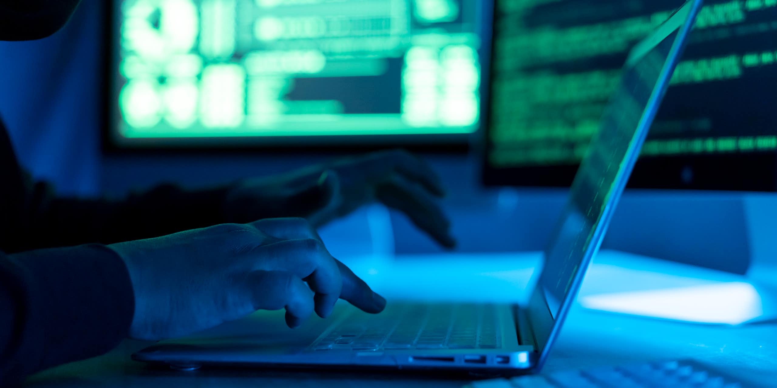 A close-up of a man typing on a computer in a dark, foreboding atmosphere.