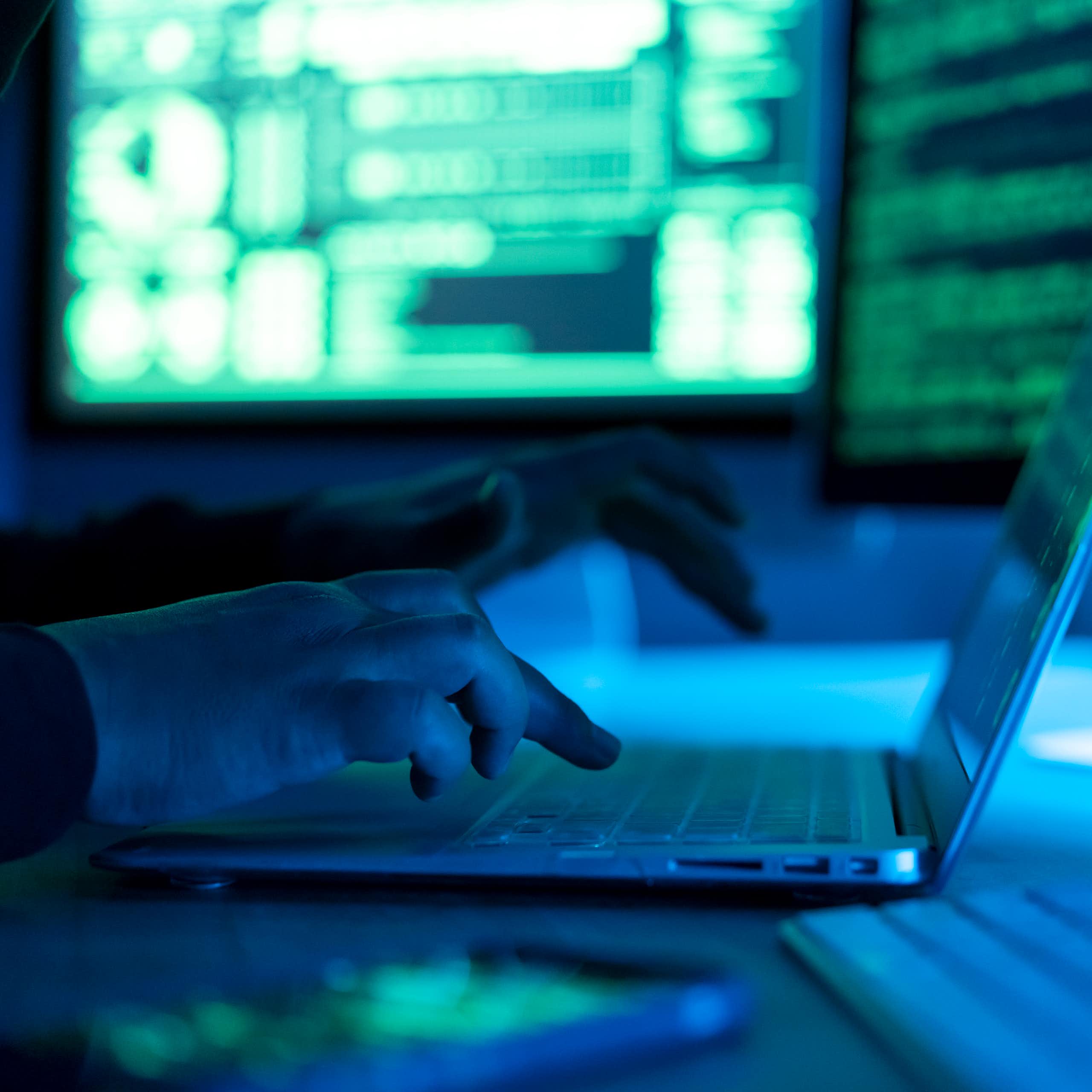 A close-up of a man typing on a computer in a dark, foreboding atmosphere.