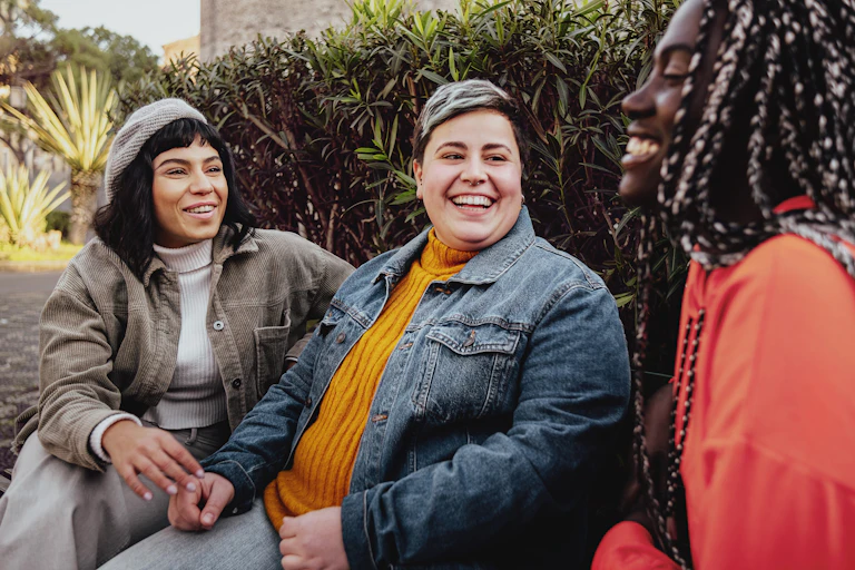 Three queer people sitting outside chat and laugh.