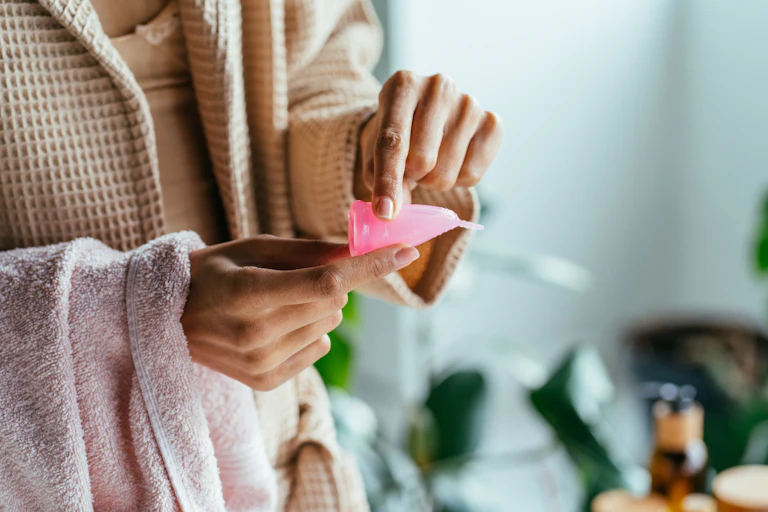 A woman bending a pink menstrual cup.