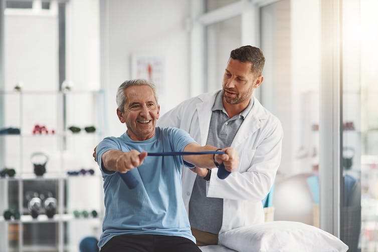 A grey-haired man using resistance bands with a physiotherapist