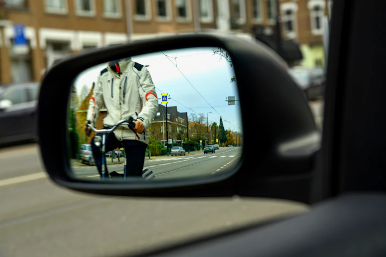A cyclist is seen in the mirror of a car.