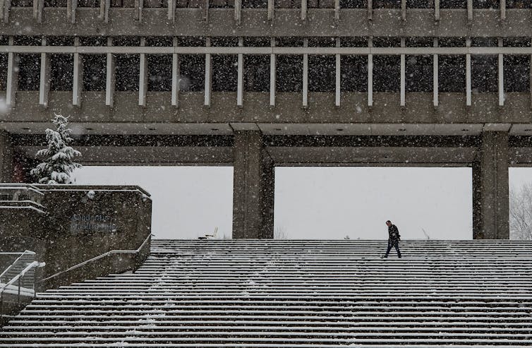 A figure crosses stairs in snow.